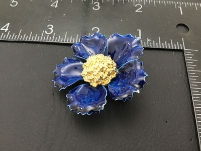 Sale Photo Thumbnail #178: A vintage flower brooch featuring glossy dark blue enamel petals with scalloped edges and a textured gold-tone stamen center. The back shows a gold-tone pin mechanism with a roll-over safety clasp and a mottled blue and white enameling on the reverse side