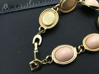 Sale Photo Thumbnail #122: Vintage  gold-tone link bracelet featuring oval light pink faux cabochons (glass or Lucite) set in bezel frames. The fold-over clasp features the recognizable Aigner 'A' horseshoe logo. Measures approximately 7.5 inches in total length. Good vintage condi