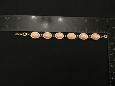 Sale Photo Thumbnail #123: Vintage  gold-tone link bracelet featuring oval light pink faux cabochons (glass or Lucite) set in bezel frames. The fold-over clasp features the recognizable Aigner 'A' horseshoe logo. Measures approximately 7.5 inches in total length. Good vintage condi