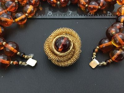 Sale Photo Thumbnail #32: Vintage multi-strand costume jewelry necklace featuring amber-tone round Lucite or resin beads with striped interior details. Includes an ornate gold-tone coiled wire centerpiece that doubles as a removable brooch/clasp piece with slide clip attachments. 