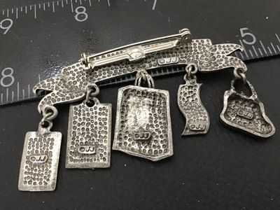 Sale Photo Thumbnail #67: A vintage silver-tone pewter novelty brooch by Jonette Jewelry (JJ) featuring a 'BORN TO SHOP' banner with five dangling shopping-themed charms: a coin purse, five-dollar bill, goody bag, 'Sale 50% Off' sign, and a credit card. Marked '©JJ' on the revers