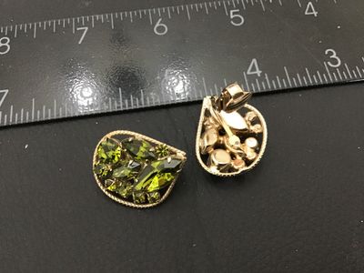 Sale Photo Thumbnail #29: Pair of vintage gold-tone clip-on earrings featuring marquise and round-cut olive green rhinestones set within a textured border. Each earring measures approximately 1 inch across. In good condition with functional clip backs and intact stones.