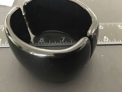 Sale Photo Thumbnail #36: A wide, glossy black acrylic or plastic hinged cuff bracelet. Features a spring hinge design for easy wear. Measures approximately 2 inches wide. Good pre-owned condition with light surface wear visible upon close inspection.