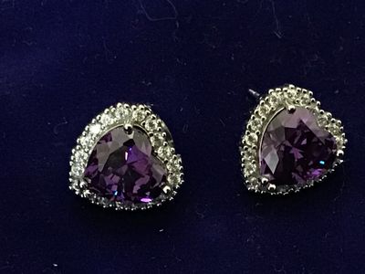 Sale Photo Thumbnail #105: Pair of silver-tone stud earrings featuring heart-cut purple central stones surrounded by a halo of clear accent stones. Secured with friction post backs. Each earring measures approximately 1/2 inch in size. Good condition with light wear.
