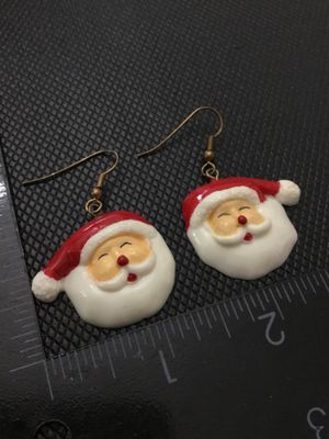Sale Photo Thumbnail #239: A pair of festive Christmas Santa Claus face dangle earrings. Made of painted resin or plastic with brass-tone French wire ear hooks. The Santa face charms measure approximately 1 inch in width and height. Pre-owned in good condition with minor surface we