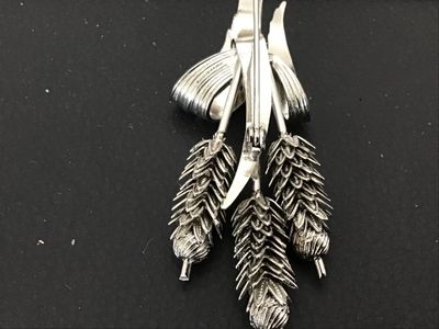 Sale Photo Thumbnail #59: A silver-tone costume jewelry brooch designed as a bundle of three wheat stalks tied with a textured ribbon motif. Features detailed textured grains and a pin-back closure on the reverse. Measures approximately 3 inches in length. In good condition with m