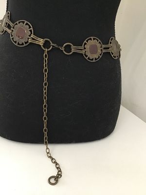 Sale Photo Thumbnail #157: Vintage brass-tone chain link belt featuring ornate openwork circular medallions inset with purple and brown glass or acrylic cabochons. Includes an adjustable hook and tail extension chain. Shows light finish wear and patina consistent with age.