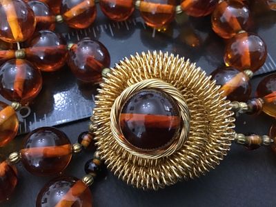Sale Photo Thumbnail #31: Vintage multi-strand costume jewelry necklace featuring amber-tone round Lucite or resin beads with striped interior details. Includes an ornate gold-tone coiled wire centerpiece that doubles as a removable brooch/clasp piece with slide clip attachments. 