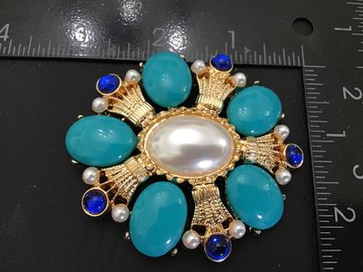 Sale Photo Thumbnail #15: Ornate gold-tone statement brooch pin featuring a large central faux pearl surrounded by teal cabochons, faux pearls, and royal blue rhinestones in a starburst/cross design. Measures approximately 2.5 inches in diameter. Features a pin back closure in wor