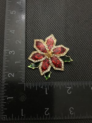 Sale Photo Thumbnail #205: A festive gold-tone holiday poinsettia brooch featuring red glitter enamel petals bordered by clear rhinestones and green enamel holly leaf accents. Marked '©TC' on the reverse side. Has a standard pin back with standard clasp function. Measures approxim