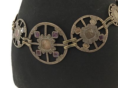 Sale Photo Thumbnail #153: Vintage brass-tone chain link belt featuring ornate openwork circular medallions inset with purple and brown glass or acrylic cabochons. Includes an adjustable hook and tail extension chain. Shows light finish wear and patina consistent with age.