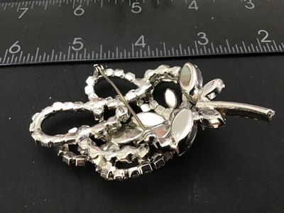 Sale Photo Thumbnail #88: Vintage silver-tone brooch featuring clear marquise and round cut rhinestones arranged in a floral floral spray and ribbon loop design. Measures approximately 2.5 inches in length. Features a rollover safety clasp on the back. Unmarked. In good vintage co