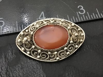 Sale Photo Thumbnail #168: Vintage fine silver-toned filigree oval brooch featuring an oval bezel-set carnelian stone or agate cabochon at the center. Intricate wirework filigree with beaded accents and a textured mesh design on the reverse. Measures approximately 1.25 inches long 