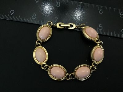 Sale Photo Thumbnail #120: Vintage  gold-tone link bracelet featuring oval light pink faux cabochons (glass or Lucite) set in bezel frames. The fold-over clasp features the recognizable Aigner 'A' horseshoe logo. Measures approximately 7.5 inches in total length. Good vintage condi