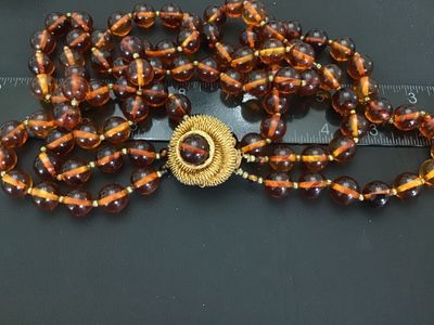 Sale Photo Thumbnail #30: Vintage multi-strand costume jewelry necklace featuring amber-tone round Lucite or resin beads with striped interior details. Includes an ornate gold-tone coiled wire centerpiece that doubles as a removable brooch/clasp piece with slide clip attachments. 