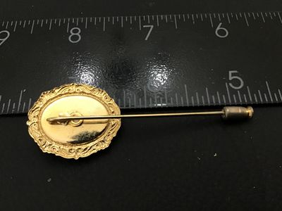 Sale Photo Thumbnail #23: Vintage stick pin featuring an oval cabochon with a scrimshaw-style illustration of a tall sailing ship surrounded by birds. Set in a gold-tone ornate filigree frame. Includes a protective pin guard end cap. Overall pin length measures approximately 2.5 i