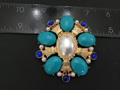 Sale Photo Thumbnail #14: Ornate gold-tone statement brooch pin featuring a large central faux pearl surrounded by teal cabochons, faux pearls, and royal blue rhinestones in a starburst/cross design. Measures approximately 2.5 inches in diameter. Features a pin back closure in wor