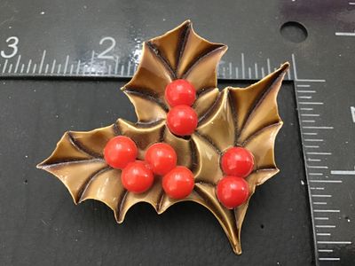 Sale Photo Thumbnail #104: Vintage Christmas brooch featuring molded tan/brown holly leaves with shiny red bead berries. Constructed from molded plastic/celluloid material with a silver-tone metal pin back mechanism. Measures approximately 2 inches wide by 1.75 inches tall. Shows m