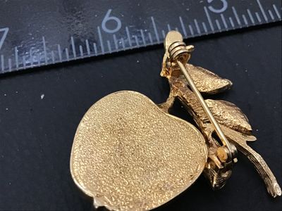 Sale Photo Thumbnail #18: A vintage Sarah Coventry gold-tone brooch shaped like an apple on a leafy branch. Features a satin iridescent pearlescent cabochon apple insert. Signed SARAH COV on the back. Pin mechanism in good working condition. Measures approximately 1.75 inches long
