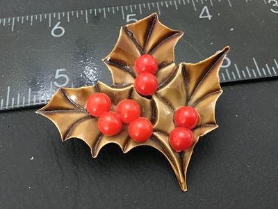 Sale Photo Thumbnail #102: Vintage Christmas brooch featuring molded tan/brown holly leaves with shiny red bead berries. Constructed from molded plastic/celluloid material with a silver-tone metal pin back mechanism. Measures approximately 2 inches wide by 1.75 inches tall. Shows m