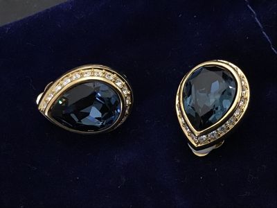 Sale Photo Thumbnail #110: Pair of vintage gold-tone clip-on earrings featuring large teardrop-cut dark blue crystal center stones surrounded by a halo of clear rhinestones. Features comfort pads on the clip backs. Measures approximately 3/4 inch in length. Items show light wear co