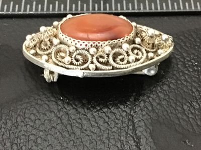 Sale Photo Thumbnail #169: Vintage fine silver-toned filigree oval brooch featuring an oval bezel-set carnelian stone or agate cabochon at the center. Intricate wirework filigree with beaded accents and a textured mesh design on the reverse. Measures approximately 1.25 inches long 