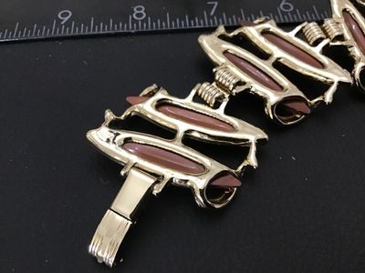 Sale Photo Thumbnail #98: Mid-century vintage gold tone link bracelet set with brown/caramel lucite or resin navette cabochons. Features sculpted scroll-like metalwork and a fold-over clasp. Measures approximately 7 inches in length. In good vintage condition with minor surface we