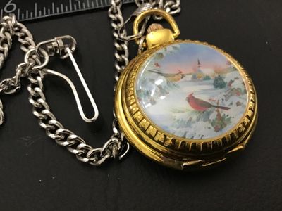 Sale Photo Thumbnail #200: Gold-tone hunter case pocket watch featuring a winter scene with a cardinal on the front cover and an ornate, detailed pattern on the back cover. The white dial displays unique, decorative stylized numerals. Includes a silver-tone chain with a belt clip. 