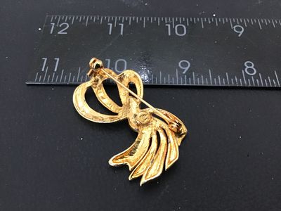 Sale Photo Thumbnail #44: A vintage gold-tone costume jewelry brooch designed as an abstract ribbon or spray bow. Features a silver-tone central band set with clear rhinestones. Shows light finish wear on the back and minor surface wear consistent with age. Measures approximately 