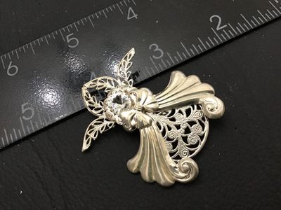 Sale Photo Thumbnail #159: A detailed silver tone vintage brooch designed in the shape of an angel with intricate openwork filigree and a central clear faceted rhinestone. Marked 'Janvis' on the reverse oval cartouche. Features a standard pin back closure. Measures approximately 2.