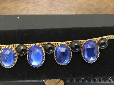 Sale Photo Thumbnail #134: Vintage gold-tone woven snake/fox tail chain bracelet featuring large faceted cobalt blue glass stones in crown prongs alternating with smooth black cabochon accent stones. Total length is approximately 7.5 inches as shown against the ruler. Metal shows l