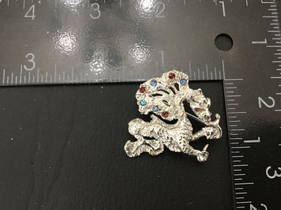 Sale Photo Thumbnail #246: Vintage Oleg Cassini dragon or mythical creature brooch pin, dated 1964 on back plaque. Textured silver-tone finish accenting blue, light blue, and red rhinestones. Measures approximately 1.75 inches across. Good vintage condition with working pin mechani