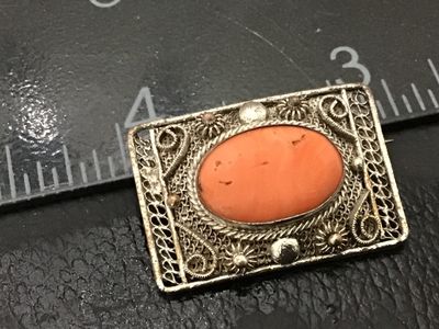 Sale Photo Thumbnail #166: An ornate vintage silver filigree brooch featuring a central oval orange coral cabochon stone surrounded by intricate wire filigree work, scrolls, and bead accents. The back features a traditional pin stem and simple catch. Shows light age-appropriate pat