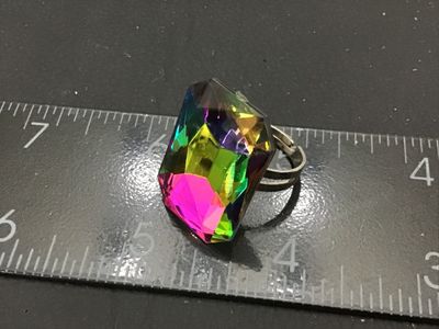 Sale Photo Thumbnail #183: Bold costume statement ring featuring a large emerald-cut iridescent rainbow crystal/glass stone on an adjustable silver-tone metal band. Shows light wear including small scratches to the top facet. Ring band is adjustable and shown measured around size 9