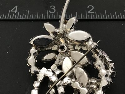 Sale Photo Thumbnail #87: Vintage silver-tone brooch featuring clear marquise and round cut rhinestones arranged in a floral floral spray and ribbon loop design. Measures approximately 2.5 inches in length. Features a rollover safety clasp on the back. Unmarked. In good vintage co