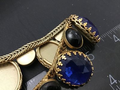 Sale Photo Thumbnail #136: Vintage gold-tone woven snake/fox tail chain bracelet featuring large faceted cobalt blue glass stones in crown prongs alternating with smooth black cabochon accent stones. Total length is approximately 7.5 inches as shown against the ruler. Metal shows l
