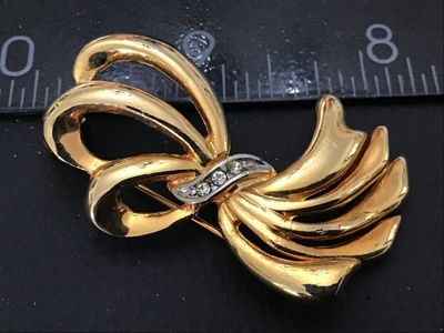 Sale Photo Thumbnail #42: A vintage gold-tone costume jewelry brooch designed as an abstract ribbon or spray bow. Features a silver-tone central band set with clear rhinestones. Shows light finish wear on the back and minor surface wear consistent with age. Measures approximately 