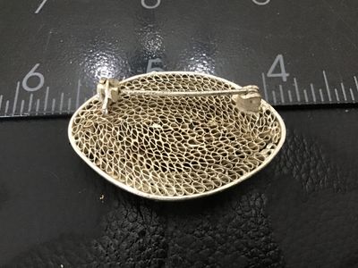 Sale Photo Thumbnail #170: Vintage fine silver-toned filigree oval brooch featuring an oval bezel-set carnelian stone or agate cabochon at the center. Intricate wirework filigree with beaded accents and a textured mesh design on the reverse. Measures approximately 1.25 inches long 