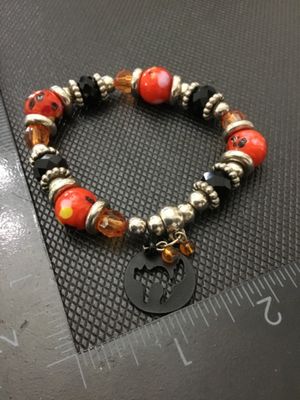 Sale Photo Thumbnail #224: Beaded stretch bracelet featuring orange and yellow spotted beads, faceted black and amber beads, silver-tone spacers, and a dangling black cat silhouette charm. Measures approximately 2.5 inches in diameter resting. In good pre-owned condition with light