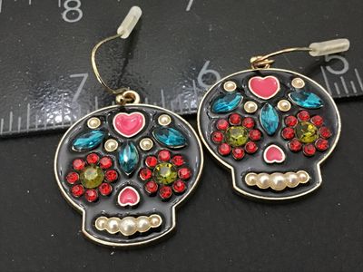 Sale Photo Thumbnail #64: Pair of gold-tone sugar skull (Calavera) dangle earrings featuring black enamel with colorful rhinestone and faux pearl accents. Equipped with french wire hooks and plastic safety backs. Skull pendants measure approximately 1 inch in width. Good condition