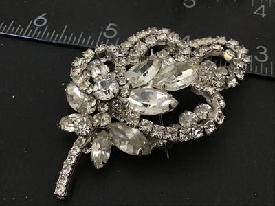 Sale Photo Thumbnail #85: Vintage silver-tone brooch featuring clear marquise and round cut rhinestones arranged in a floral floral spray and ribbon loop design. Measures approximately 2.5 inches in length. Features a rollover safety clasp on the back. Unmarked. In good vintage co