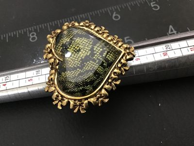 Sale Photo Thumbnail #9: A signed Betsey Johnson costume jewelry ring featuring a large heart-shaped focal piece with a faceted cover and dark pattern underneath, surrounded by a gold-tone ornate bow and heart border. The inside band is stamped 'Betsey Johnson' and set with a sig
