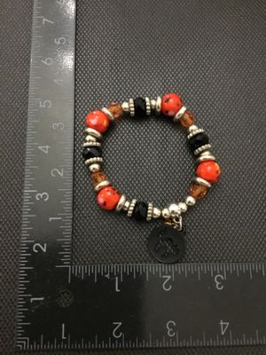 Sale Photo Thumbnail #223: Beaded stretch bracelet featuring orange and yellow spotted beads, faceted black and amber beads, silver-tone spacers, and a dangling black cat silhouette charm. Measures approximately 2.5 inches in diameter resting. In good pre-owned condition with light