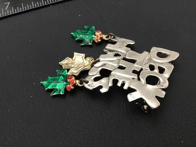 Sale Photo Thumbnail #129: Vintage Christmas holiday brooch featuring the text 'DECK THE HALLS' in a silver-tone finish with dangling green enamelled holly leaf charms accented by red rhinestones. Includes a standard pin back with locking clasp. Measures approximately 2 inches tall