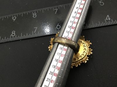Sale Photo Thumbnail #10: A signed Betsey Johnson costume jewelry ring featuring a large heart-shaped focal piece with a faceted cover and dark pattern underneath, surrounded by a gold-tone ornate bow and heart border. The inside band is stamped 'Betsey Johnson' and set with a sig