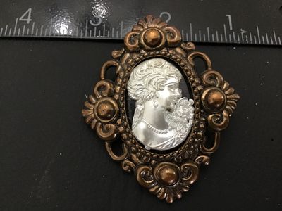 Sale Photo Thumbnail #41: Vintage brooch pin featuring a silver-tone/pewter-style woman's portrait cameo set in an ornate bronze-tone Faux metal frame with scrolling openwork design. The reverse shows a glued-on bar pin back mechanism. Measures approximately 2 inches tall by 1.5 i