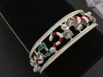Sale Photo Thumbnail #184: Silver-tone hinged cuff bangle bracelet featuring holiday-themed enamel motifs including Christmas stockings and candy canes, accented with clear rhinestones and imitation pearls. Measures approximately 2.5 inches in diameter with a spring hinge closure. 