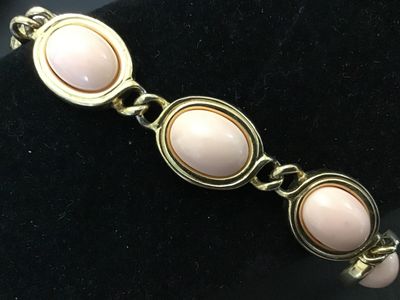 Sale Photo Thumbnail #121: Vintage  gold-tone link bracelet featuring oval light pink faux cabochons (glass or Lucite) set in bezel frames. The fold-over clasp features the recognizable Aigner 'A' horseshoe logo. Measures approximately 7.5 inches in total length. Good vintage condi