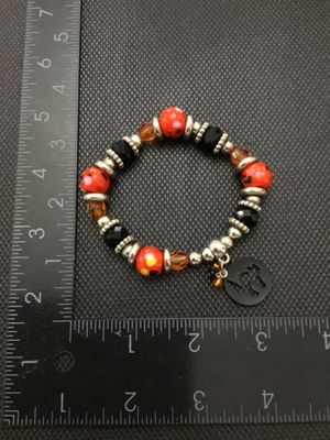 Sale Photo Thumbnail #222: Beaded stretch bracelet featuring orange and yellow spotted beads, faceted black and amber beads, silver-tone spacers, and a dangling black cat silhouette charm. Measures approximately 2.5 inches in diameter resting. In good pre-owned condition with light