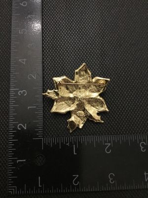 Sale Photo Thumbnail #207: A festive gold-tone holiday poinsettia brooch featuring red glitter enamel petals bordered by clear rhinestones and green enamel holly leaf accents. Marked '©TC' on the reverse side. Has a standard pin back with standard clasp function. Measures approxim